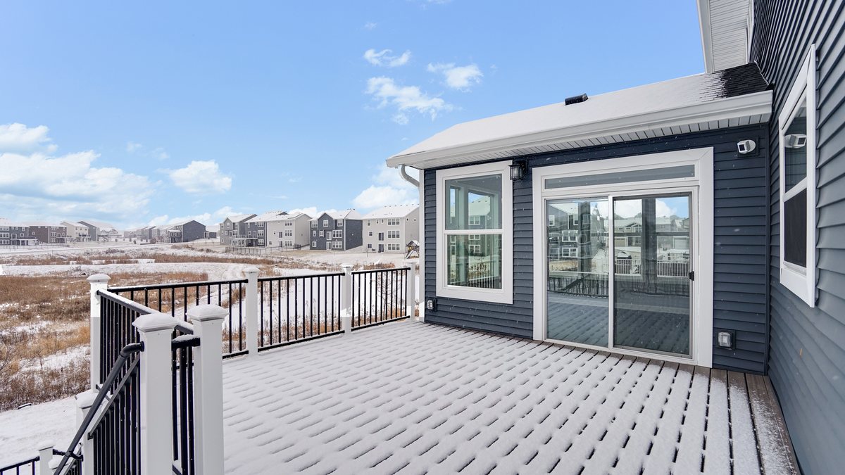 A raised composite deck with black metal balusters overlooking an open back yard.