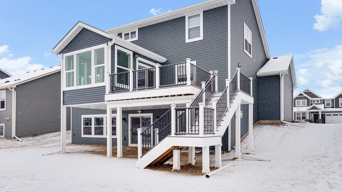 A two-story rear elevation in snow, with white gutters, downspouts and downspout extensions carrying water away from the foundation.
