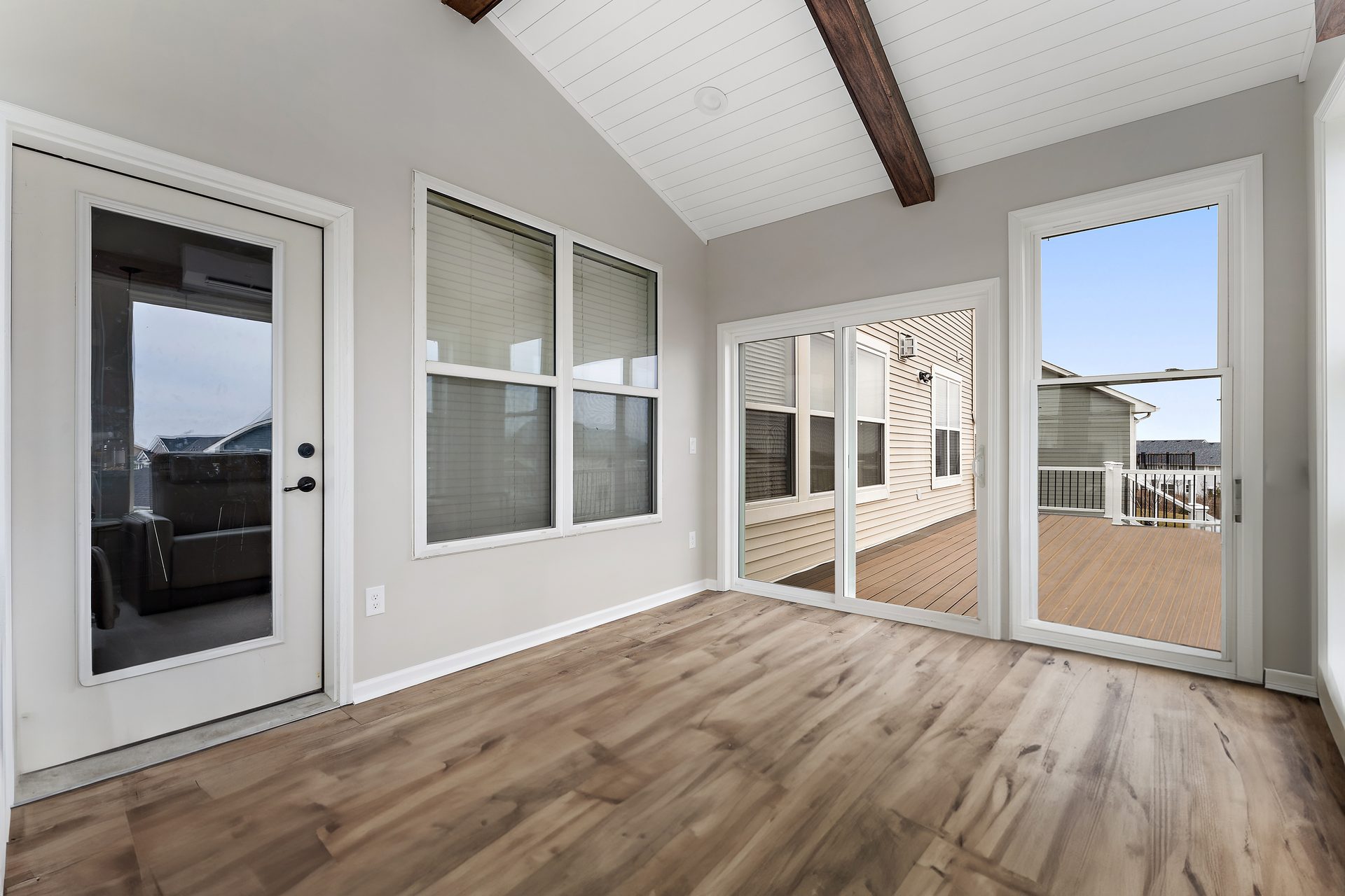 Addition interior with a vaulted shiplap ceiling, stained beams and wide-plank flooring, opening to a deck through sliding doors