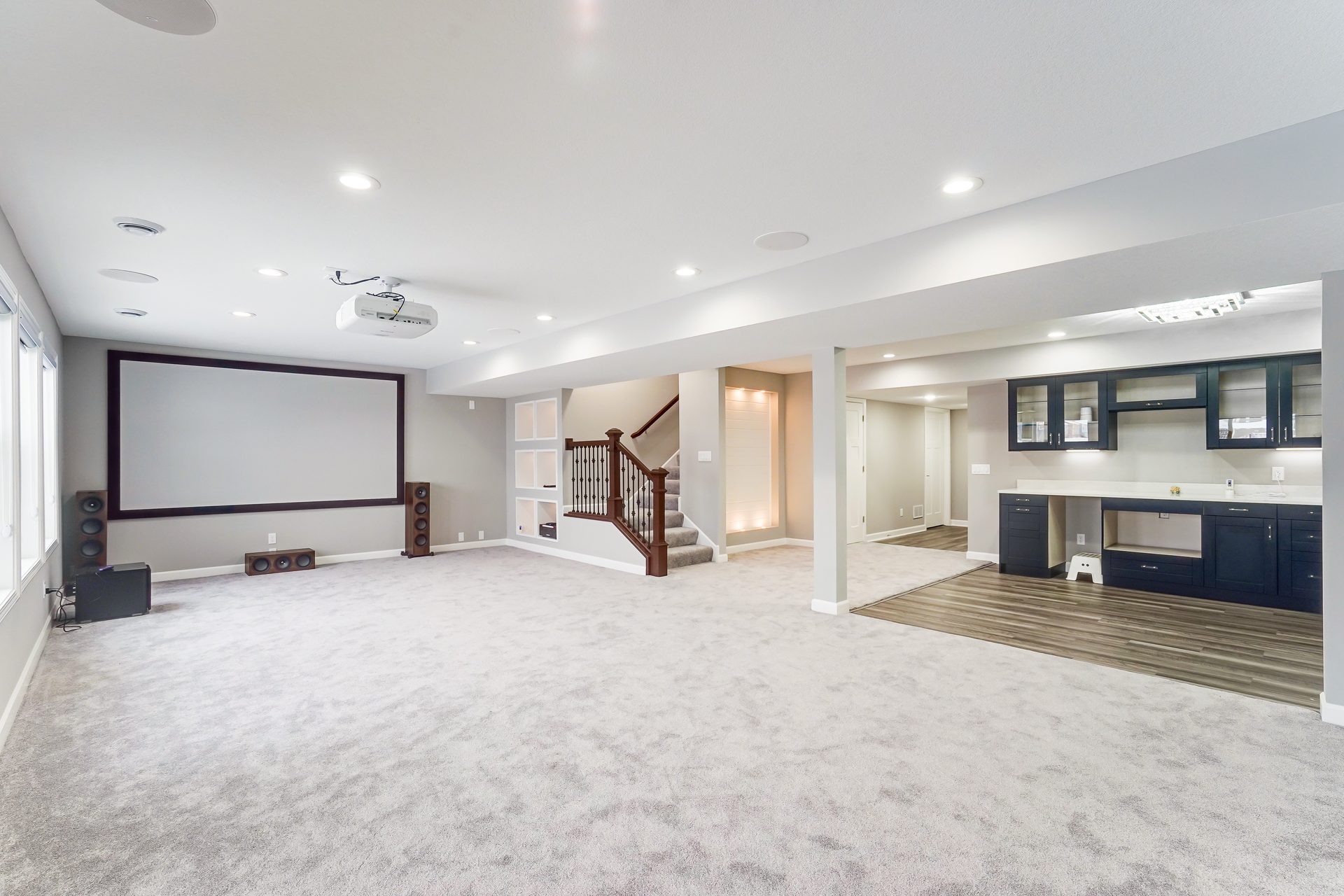 Finished lower level with a projection screen, carpet and a painted staircase with white balusters