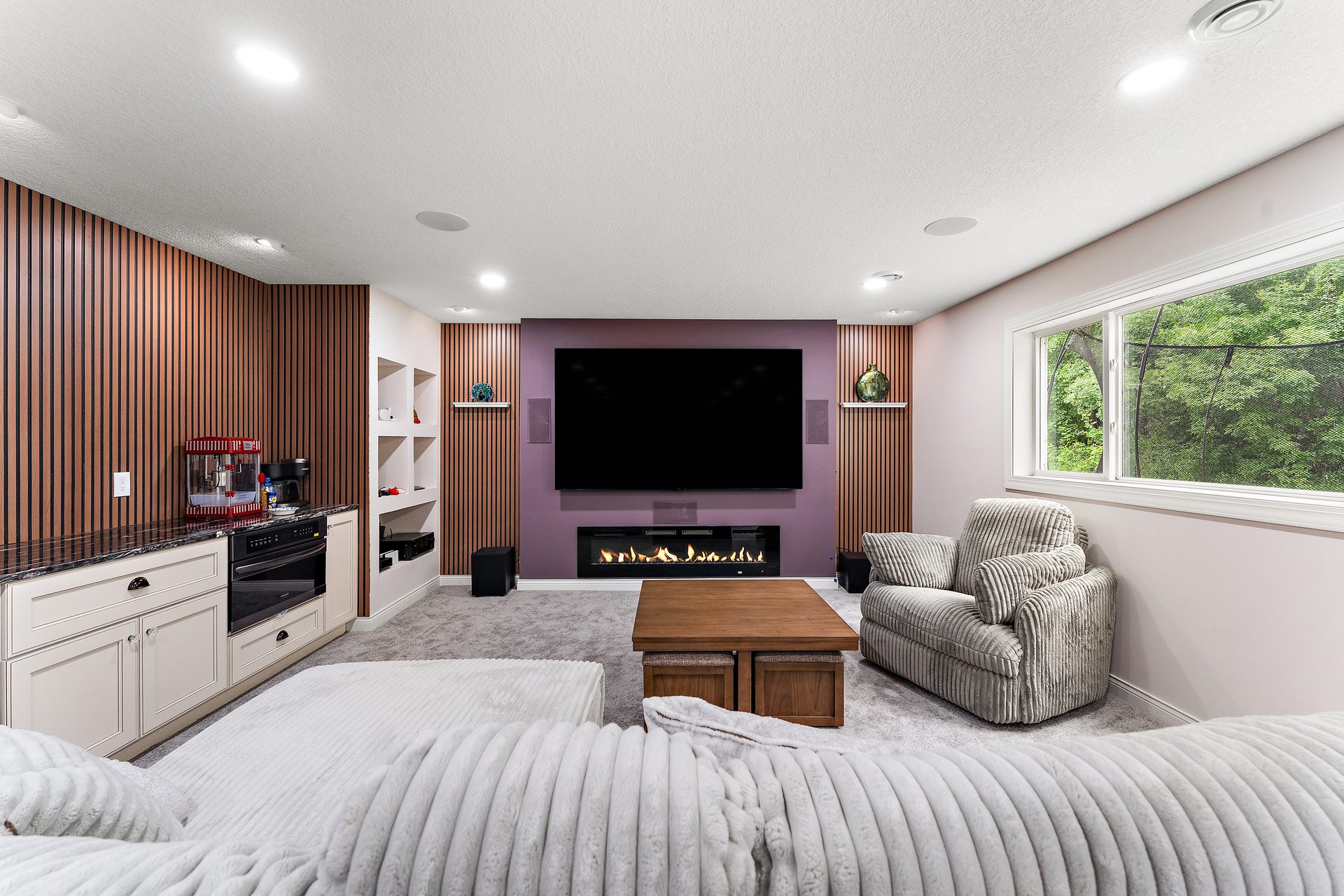 Basement living area with a vertical slat feature wall, a linear fireplace and built-in white cabinetry