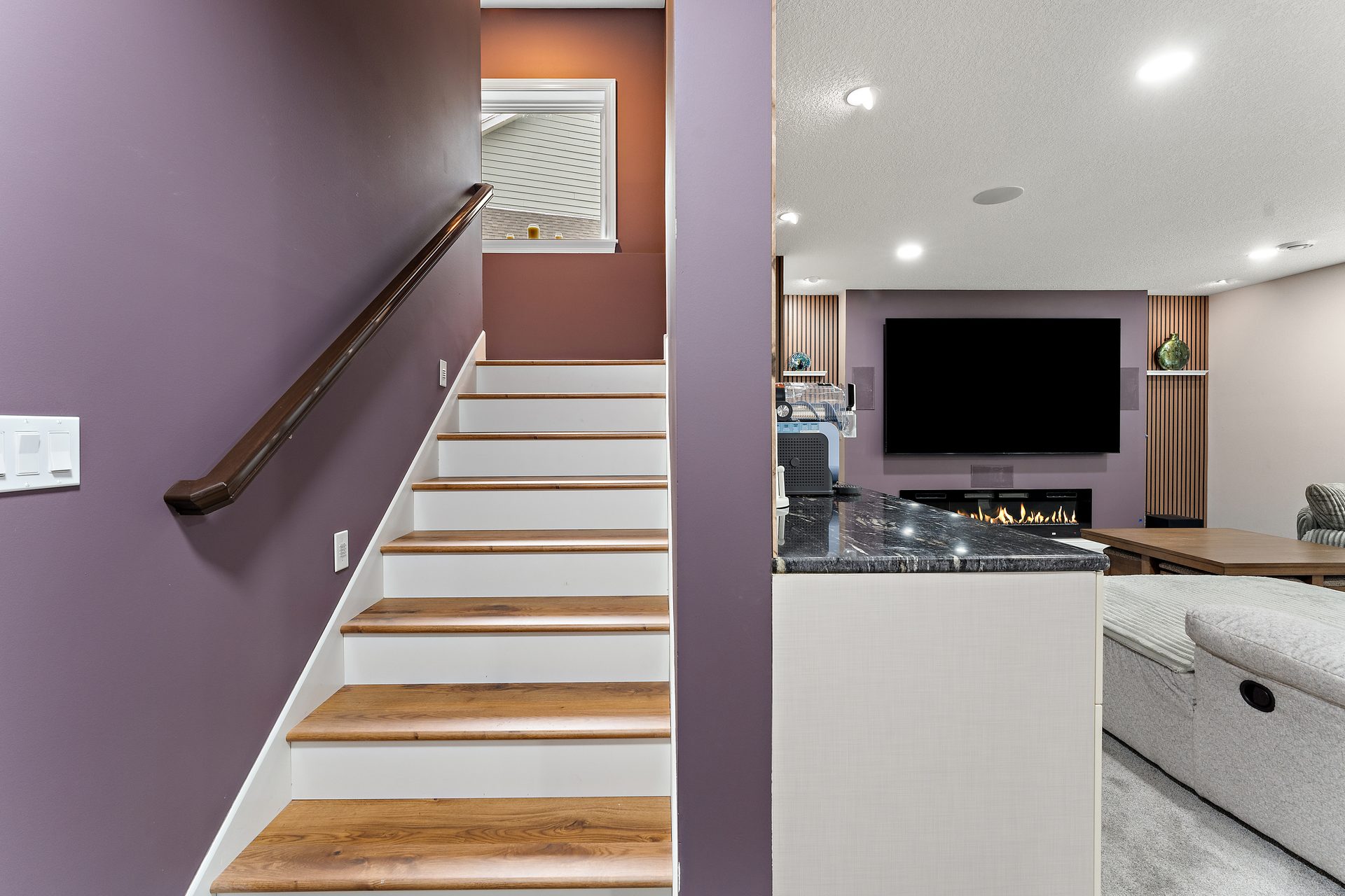 Basement staircase with white risers, stained oak treads and a wood handrail against a plum accent wall