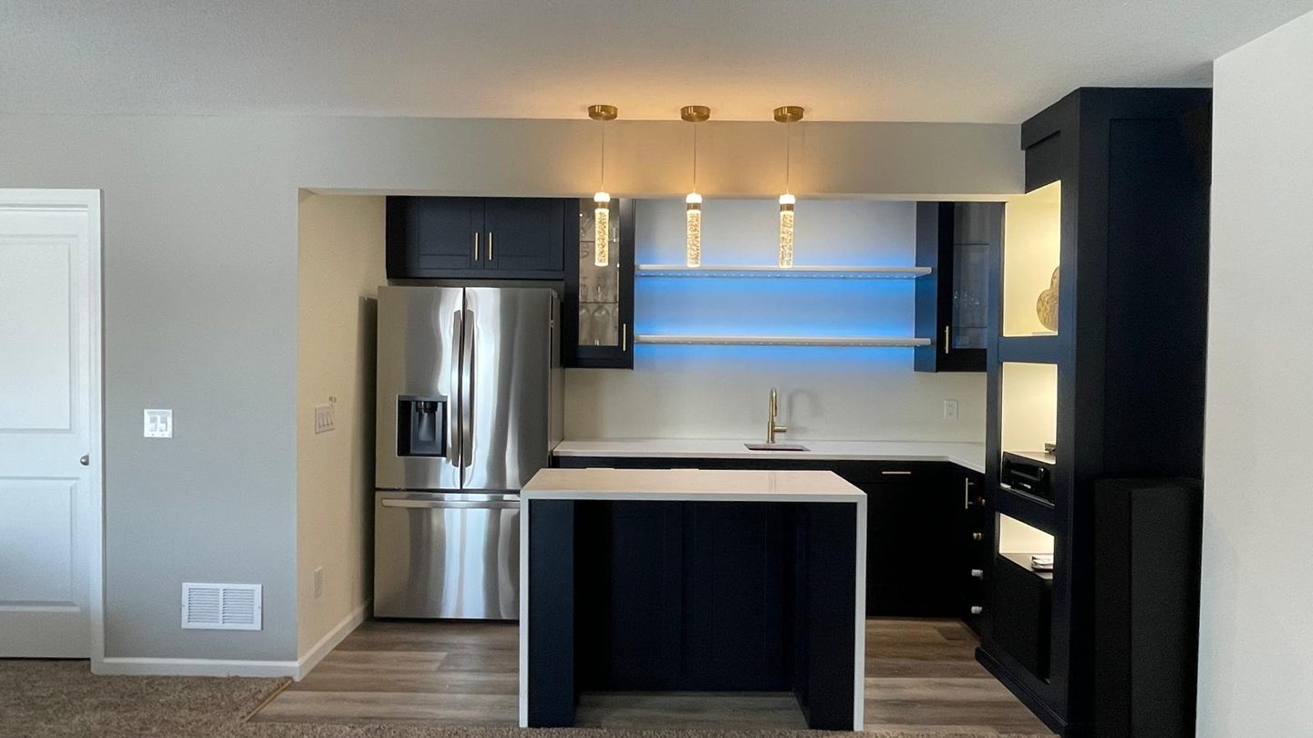 Basement kitchenette with navy cabinets, a stainless refrigerator and a quartz island under pendant lighting