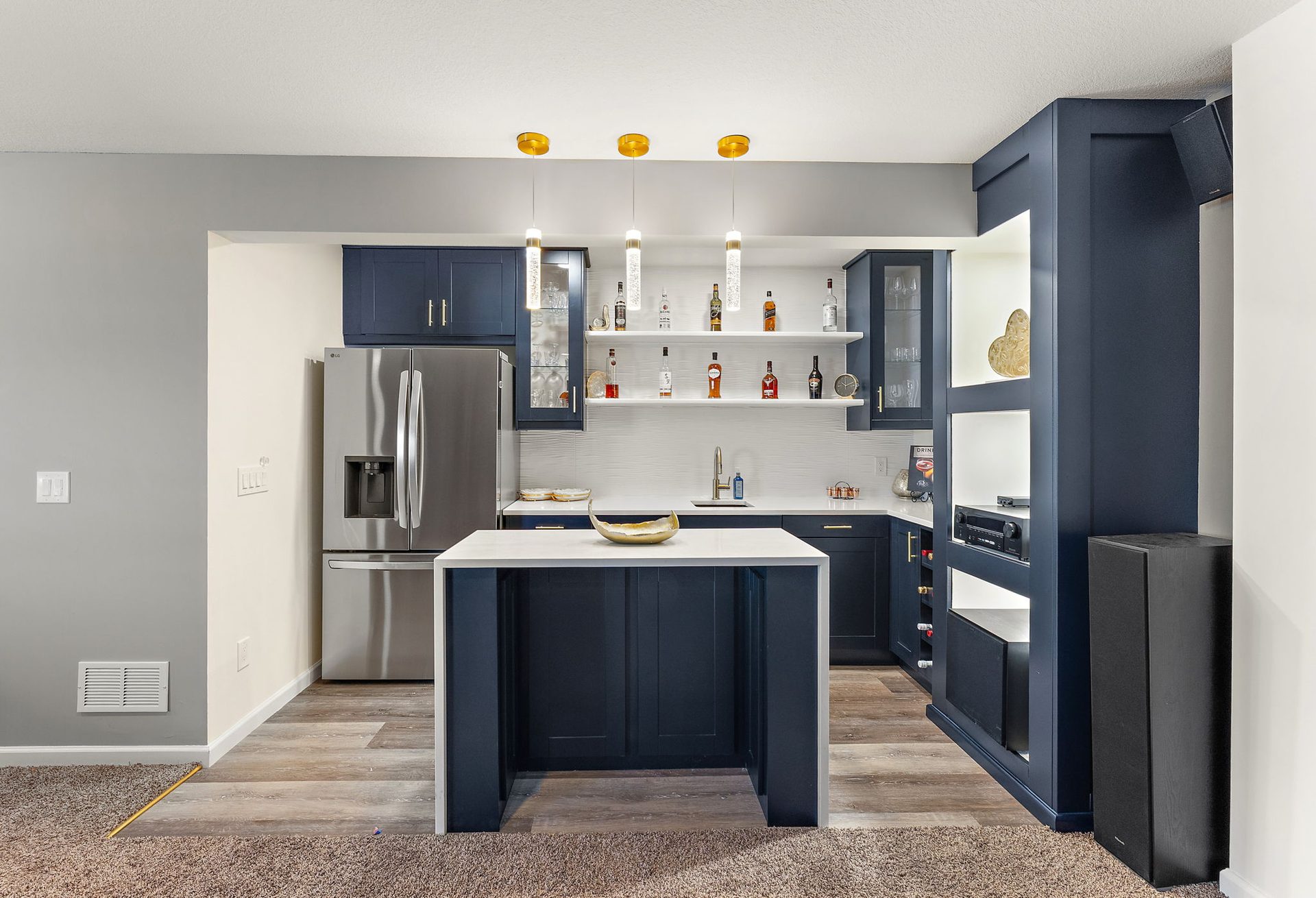 Basement wet bar with navy cabinetry, glass-front uppers and an island, where carpet meets plank flooring
