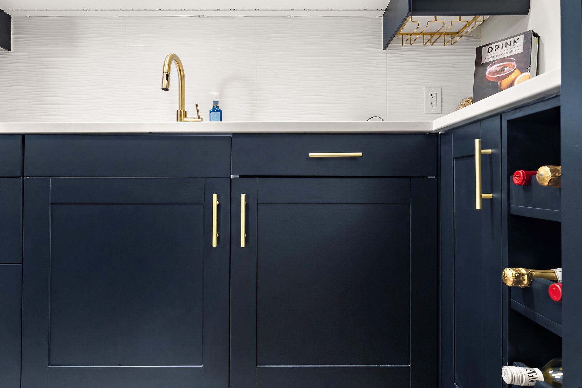 Wet bar detail with navy cabinetry, brass hardware and open bottle storage