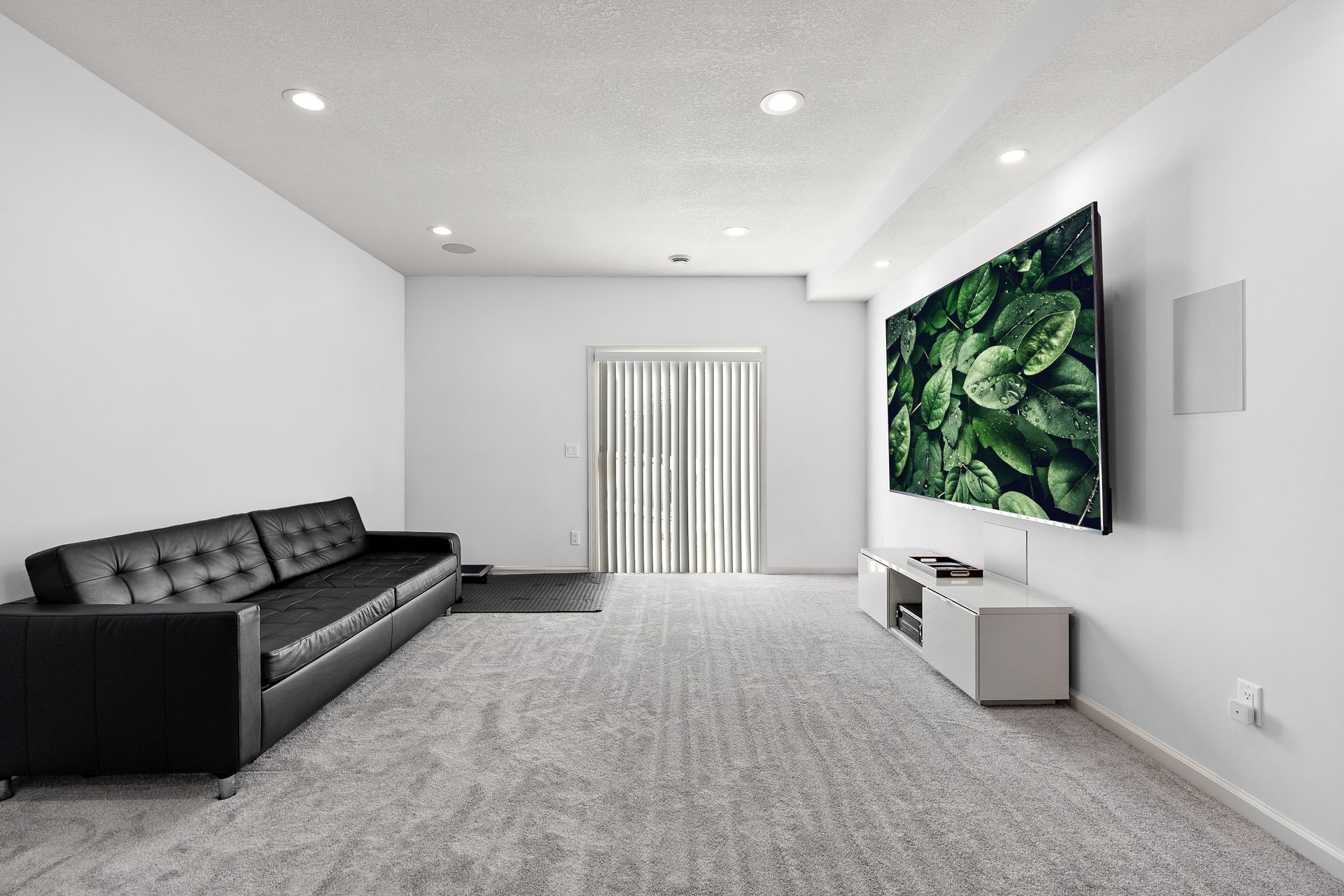 A finished basement media room with a wall-mounted screen, built-in cabinet and carpet, opening to a walkout patio door