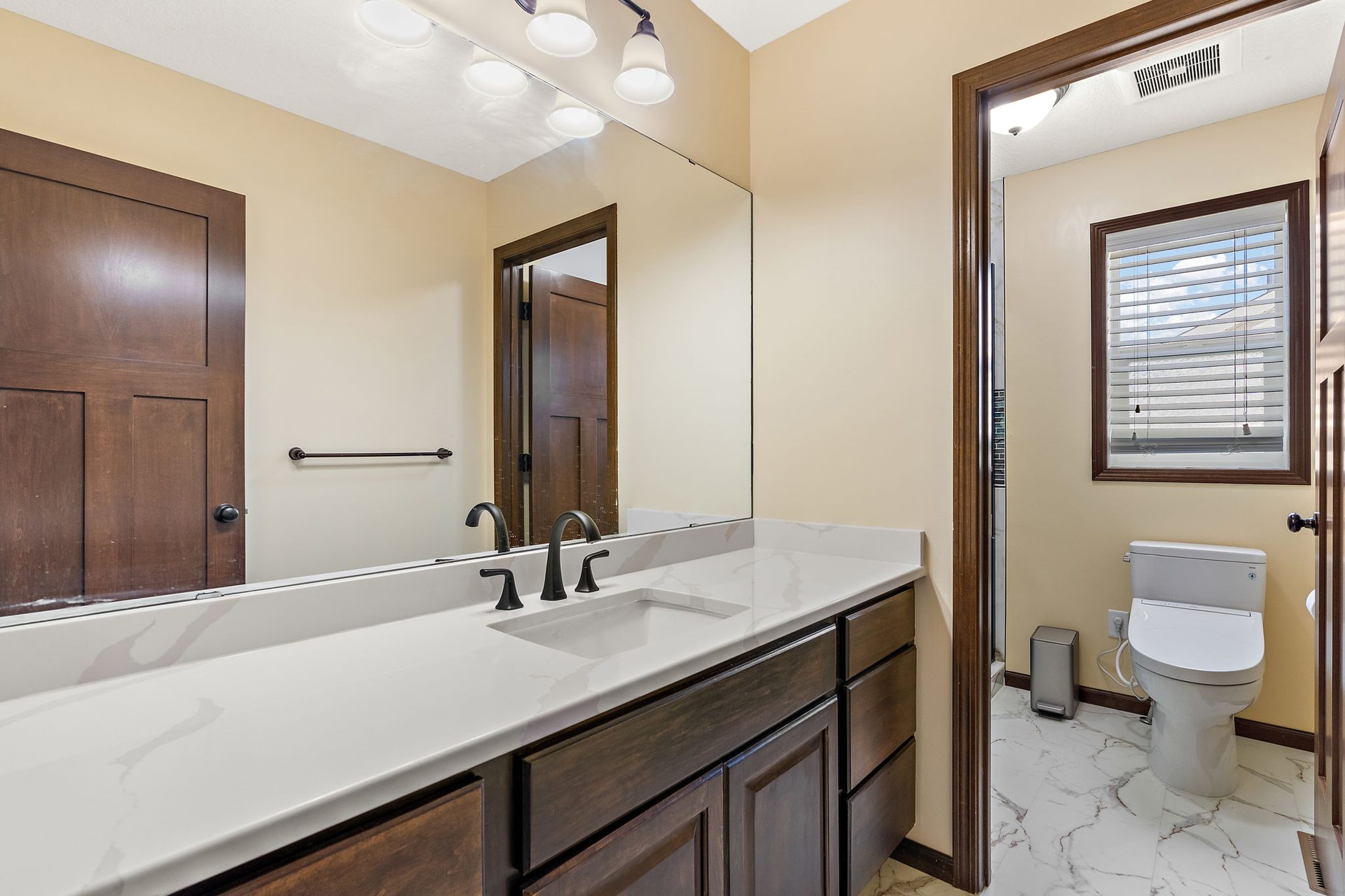 Bathroom vanity with stained cabinetry, a quartz top and a full-width mirror, with marble-look floor tile