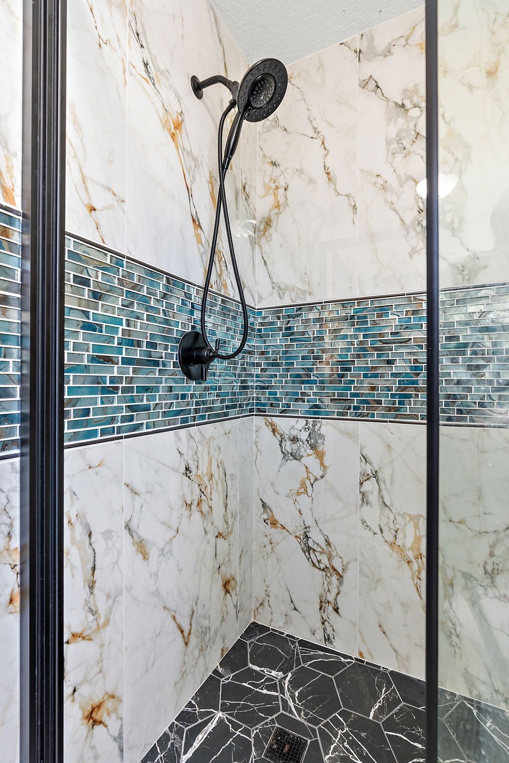 Walk-in shower with marble-look large-format tile, a glass mosaic accent band and matte black fittings