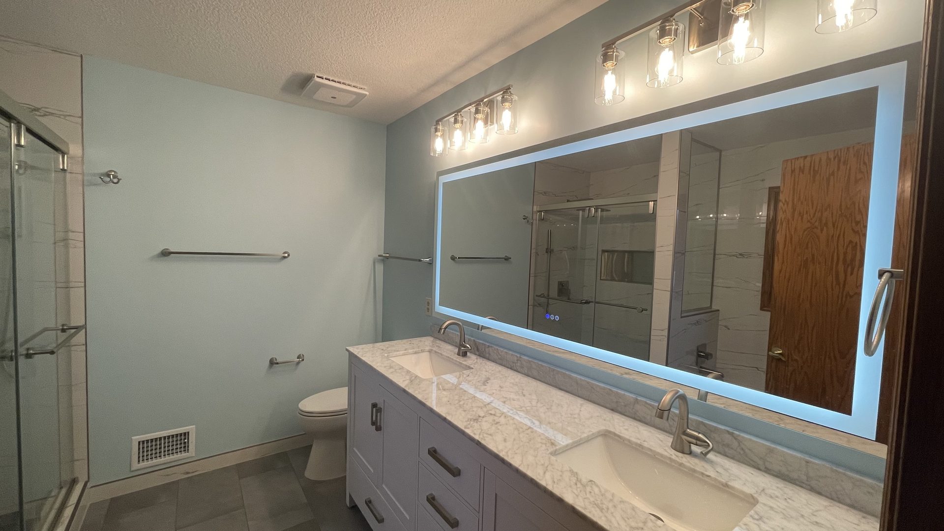Remodeled bathroom with a double vanity, a backlit mirror and a glass shower enclosure