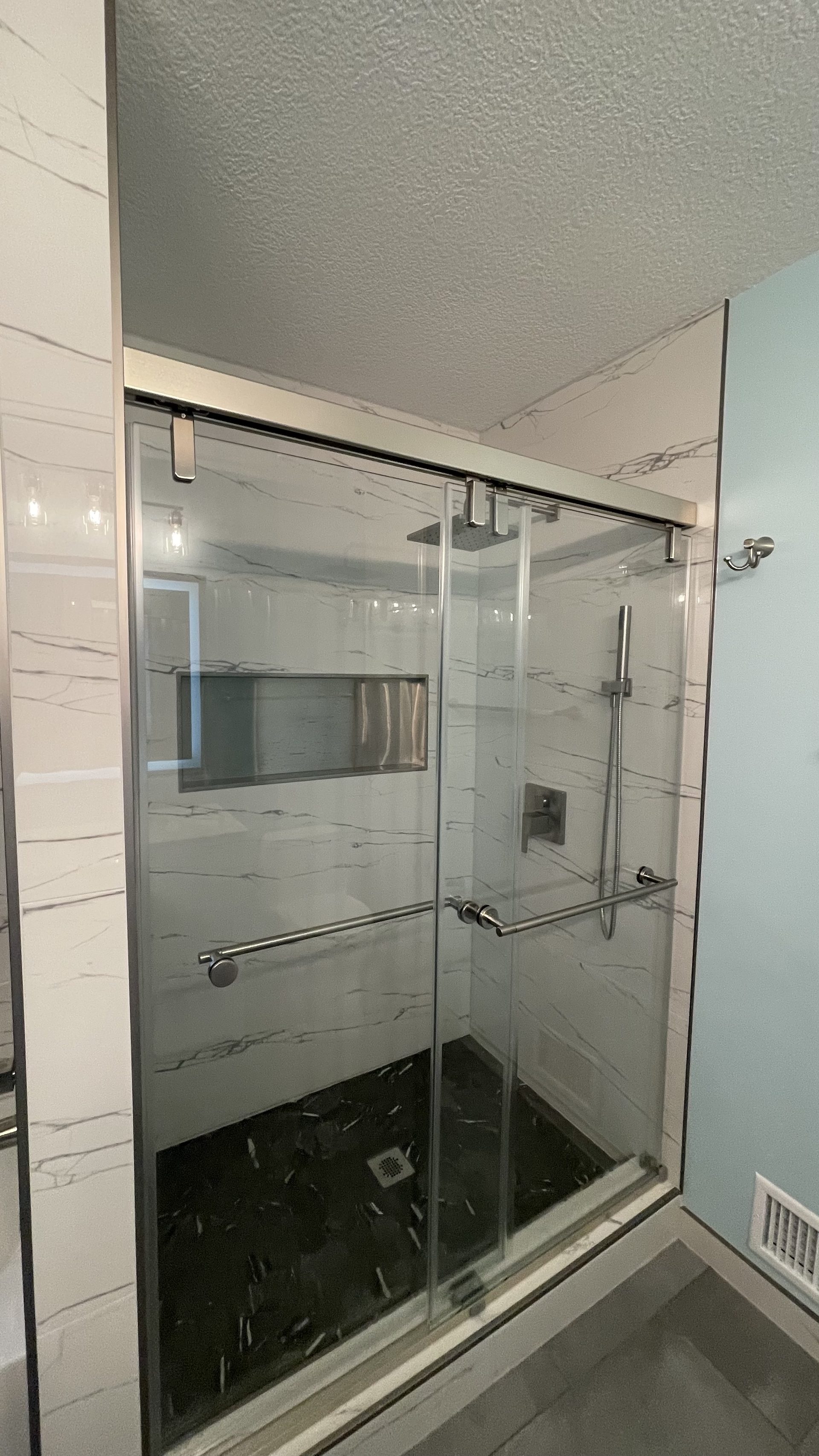 Sliding glass shower enclosure with marble-look wall tile and a dark speckled shower floor