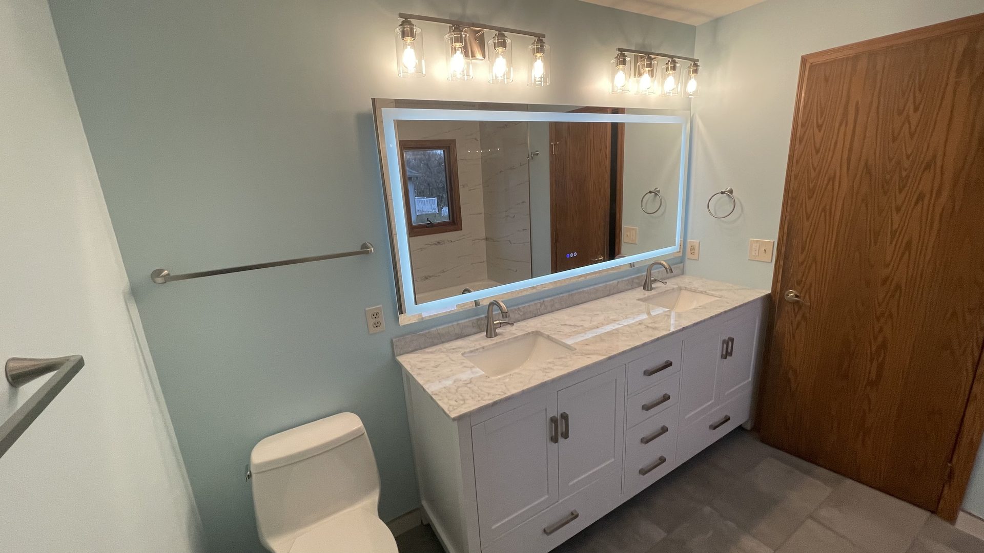 Bathroom with a white double vanity, backlit mirror and exposed-bulb vanity lighting