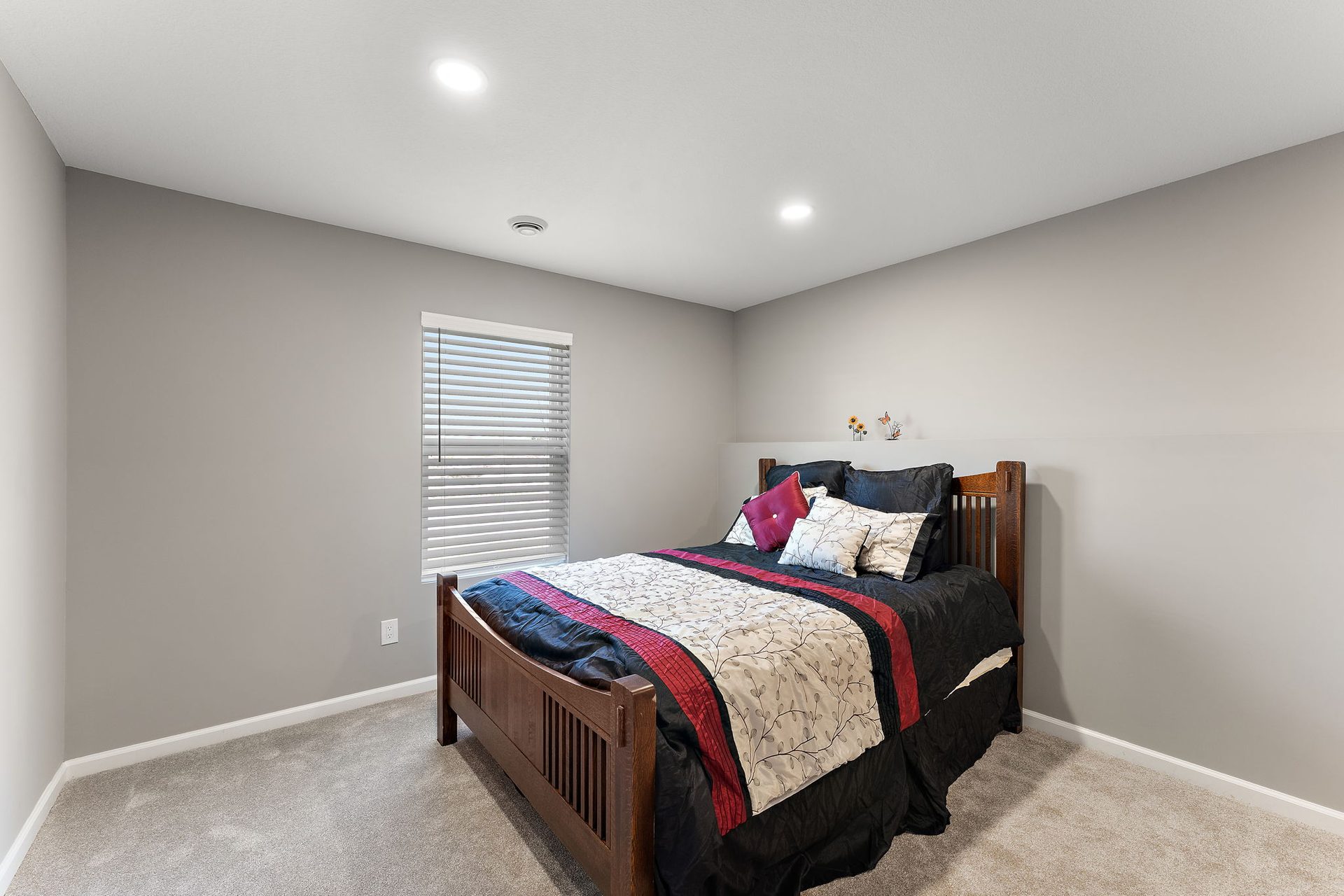 Finished bedroom with a wooden bed frame, carpet and a blind-fitted window