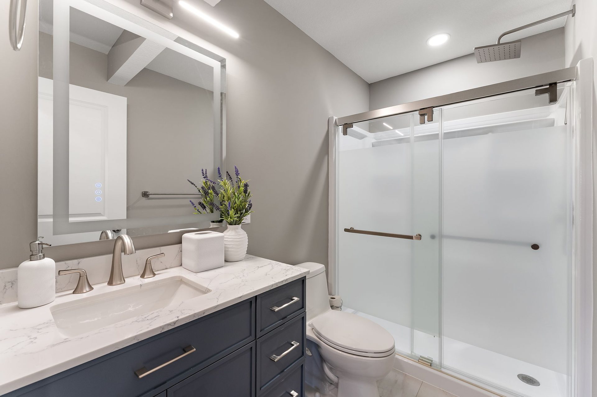 Bathroom with a navy vanity, a quartz top, a framed mirror and a sliding frosted-glass shower enclosure