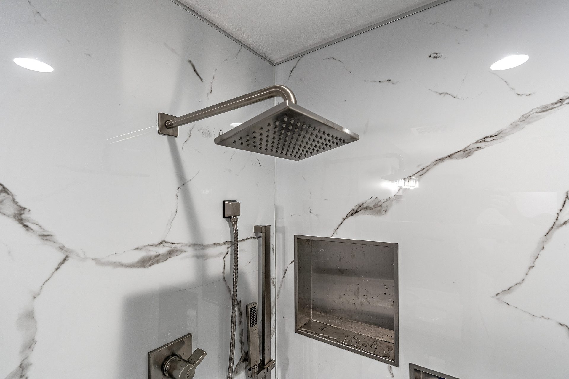 A shower interior in large-format marble-look tile, with a rain head, hand shower and a recessed niche