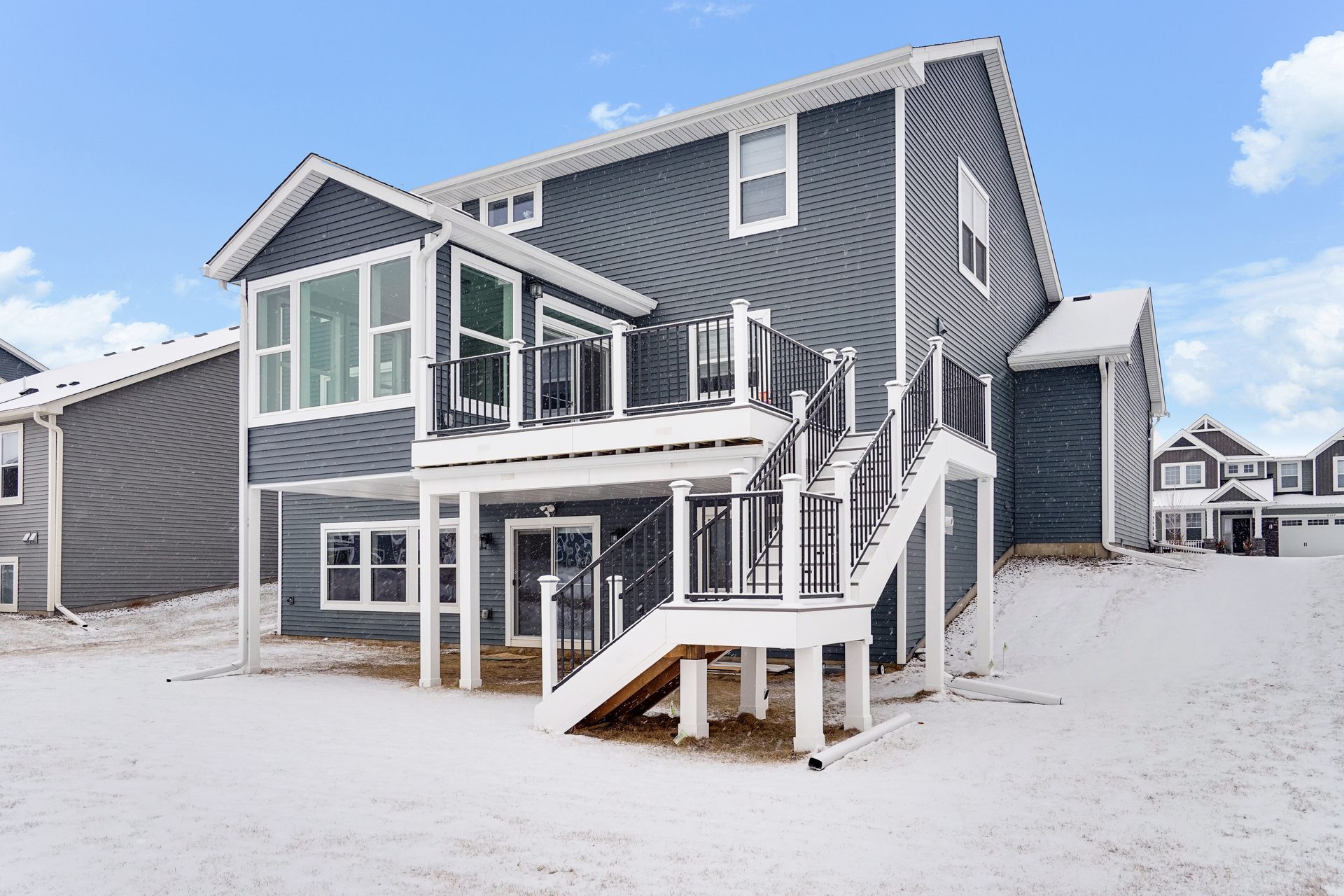 Two-story rear elevation with an elevated deck, white guard and a full flight of stairs to grade, in snow