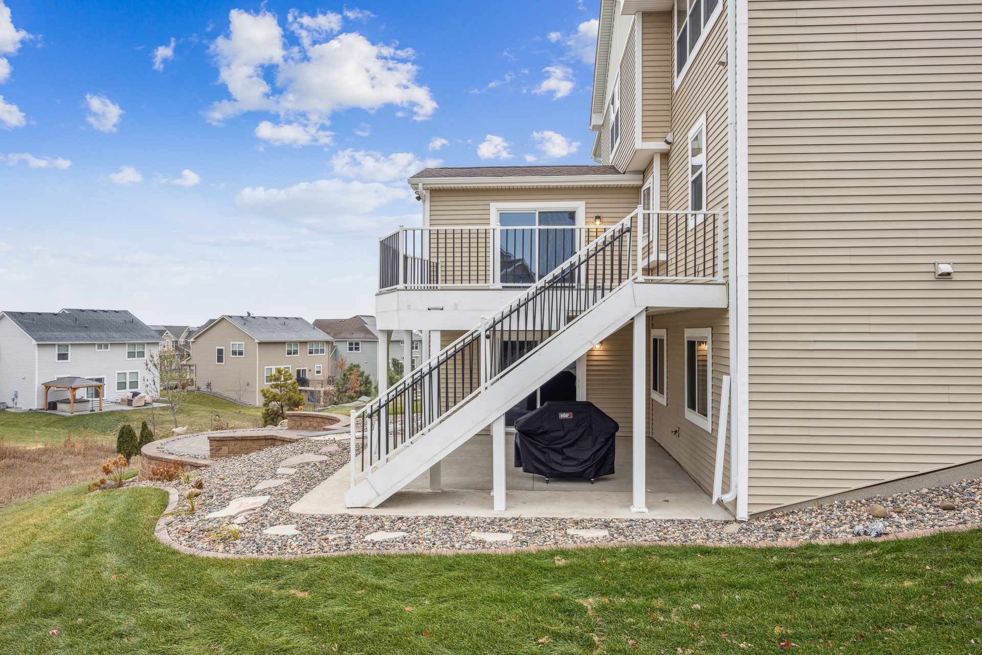 Elevated deck with white stairs to grade and a covered area beneath, above a lawn