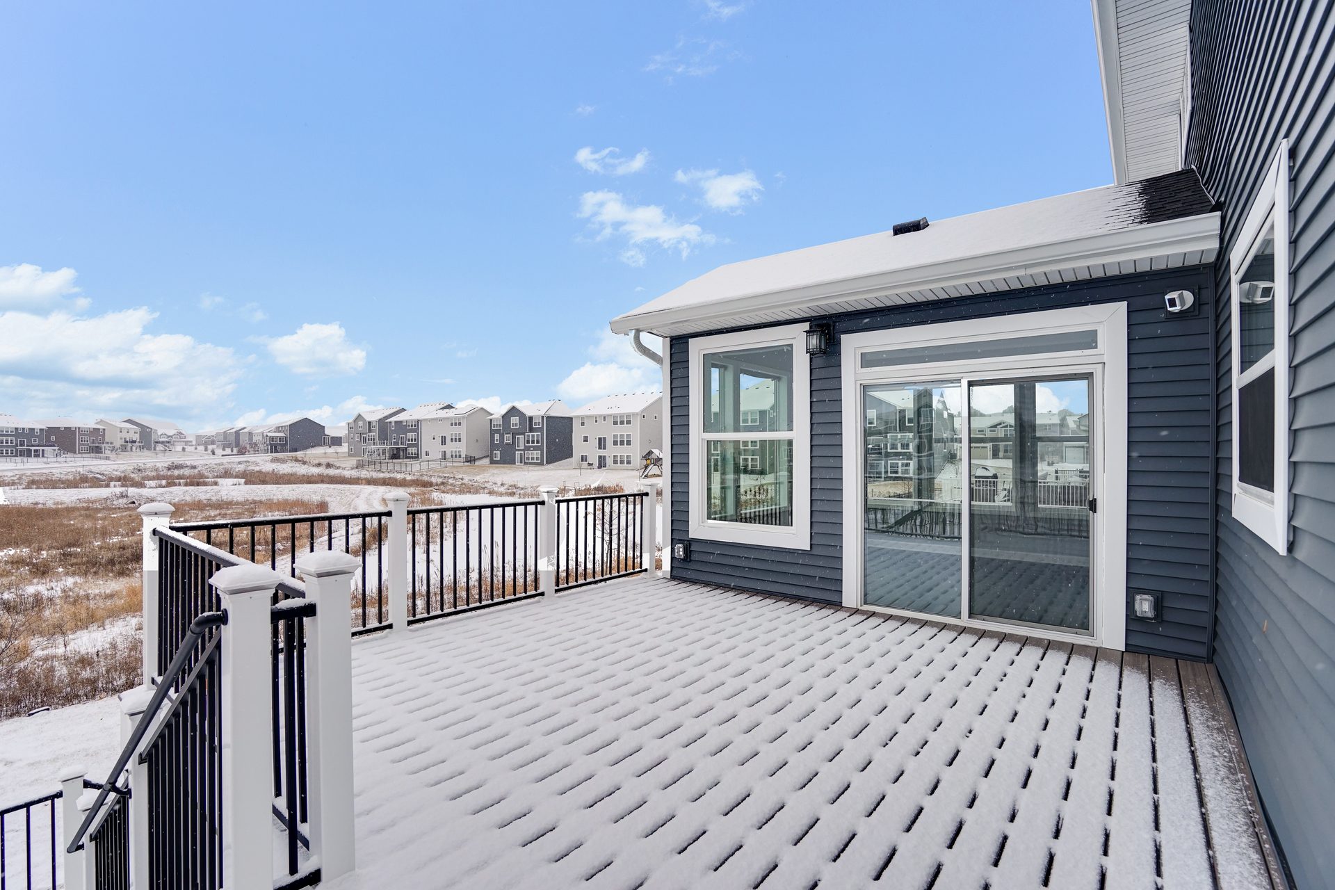 Gray composite deck at sliding doors with a black metal guard, looking over open ground in winter