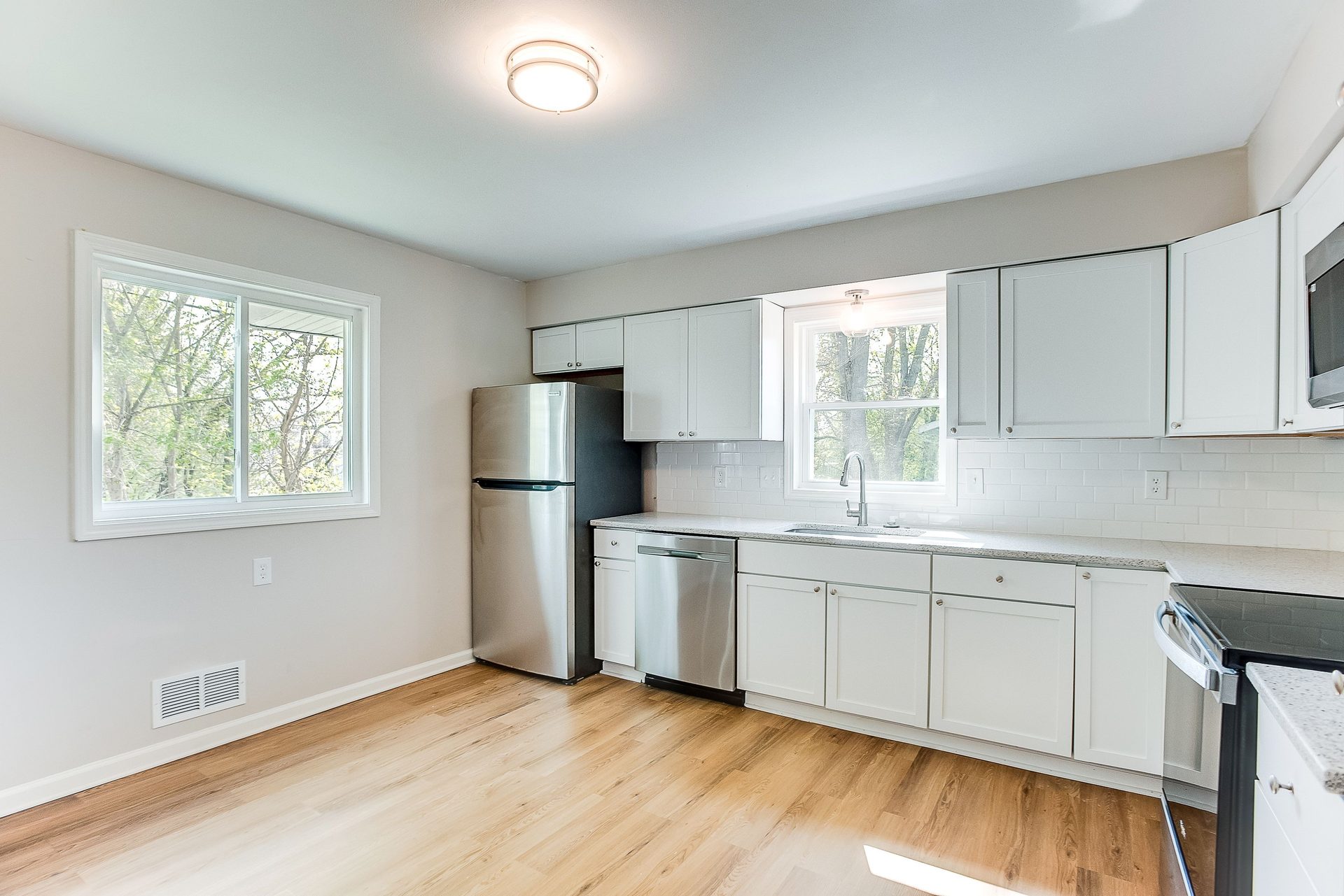 Kitchen with white shaker cabinetry, a subway tile backsplash, stainless appliances and light oak flooring