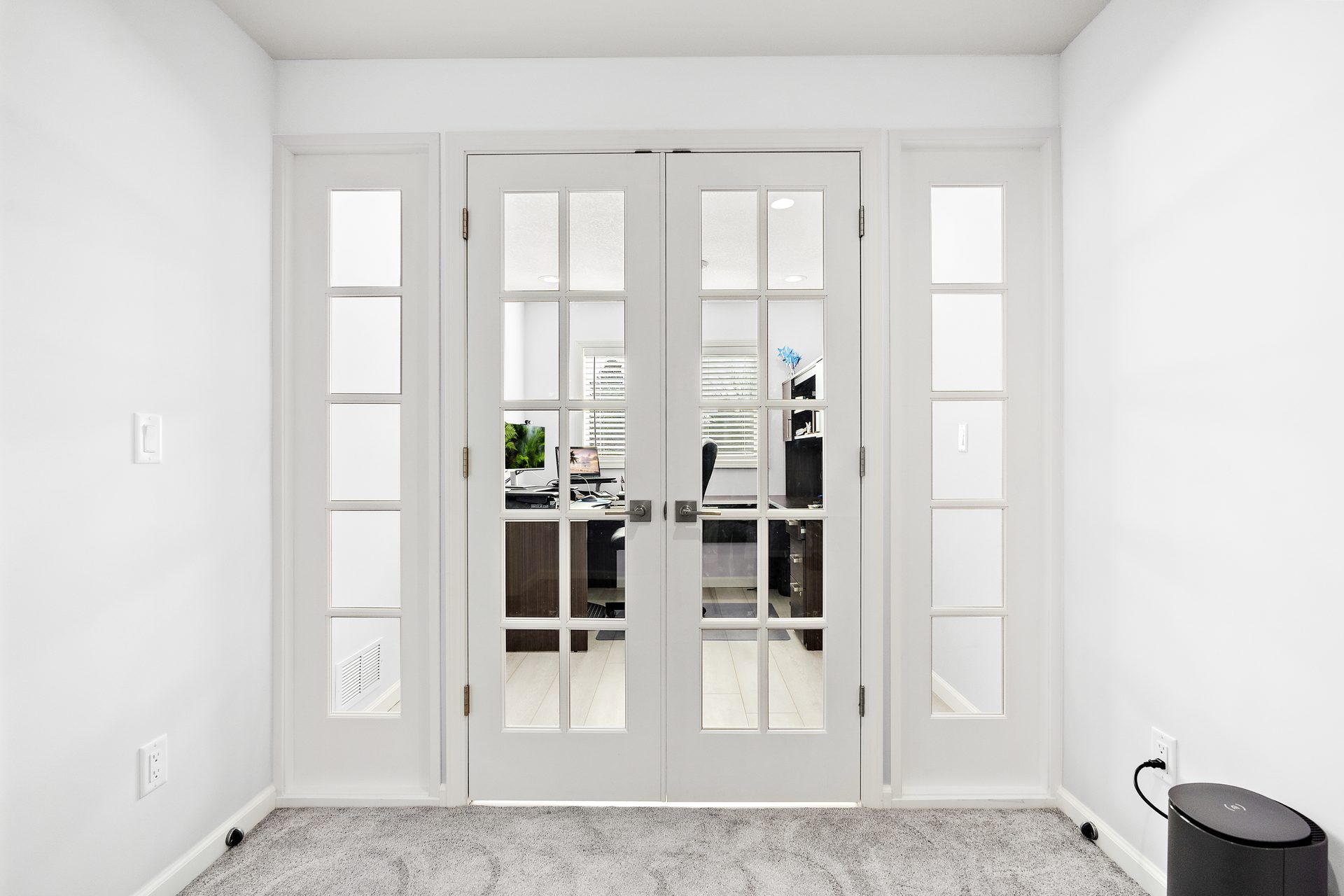 Glazed double doors with a painted surround opening from a carpeted hall into a home office