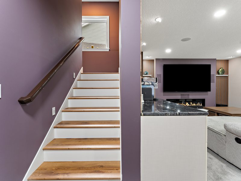 A finished lower level stair with painted risers and a wood handrail.
