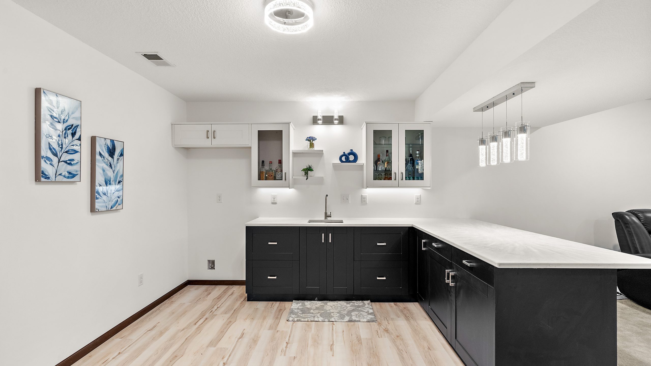 A finished basement wet bar with dark cabinetry, a quartz counter and pendant lighting.
