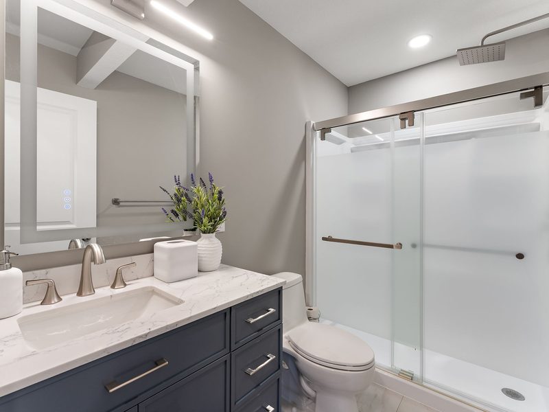 A bathroom with a navy vanity, a quartz top and a sliding frosted-glass shower enclosure.