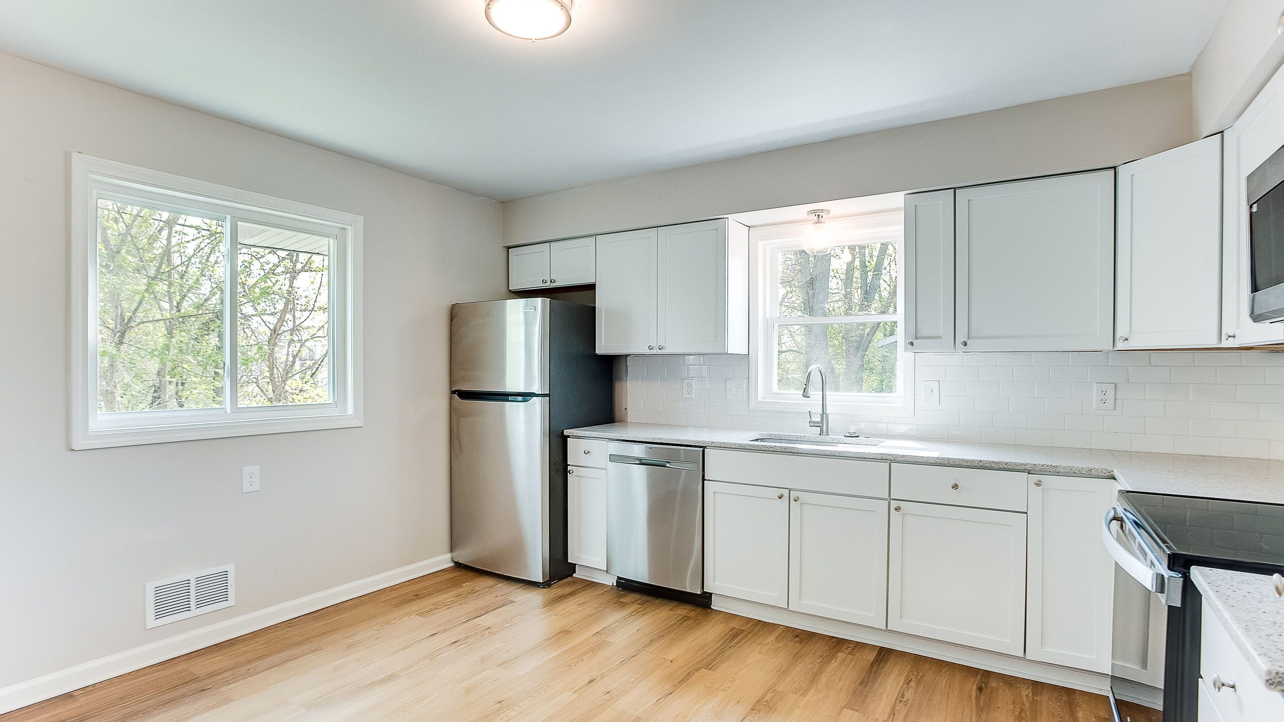 A kitchen with white shaker cabinetry, a subway tile backsplash, stainless appliances and light oak flooring.